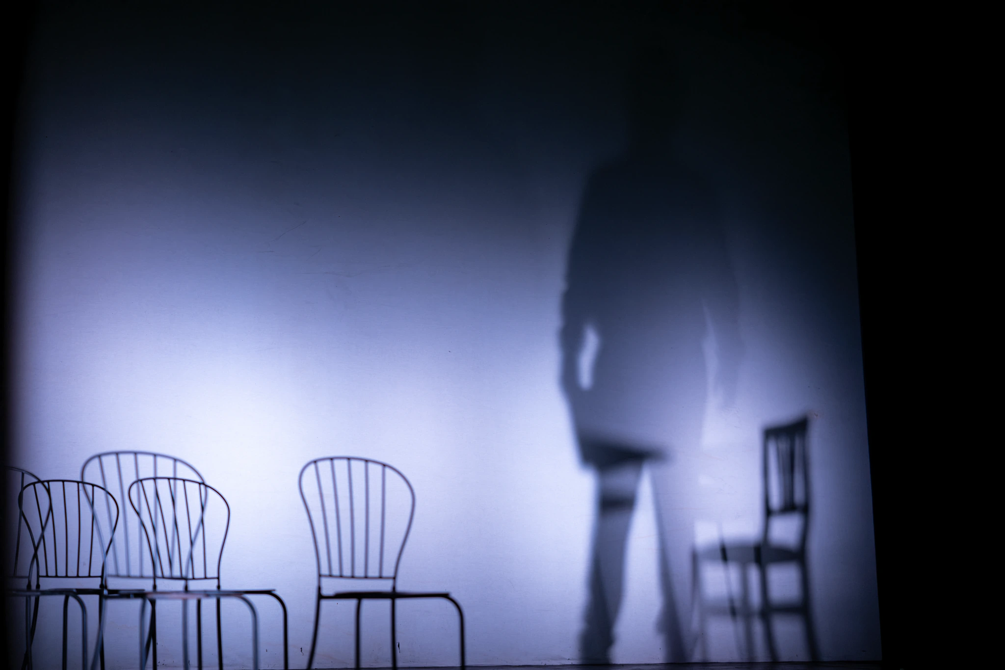 Ombra di un uomo e sedie vuote proiettate su un telo bianco, fotografia di scena
